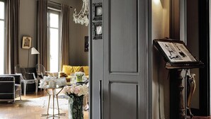 A spacious living area with a large dark wooden door, a chandelier, and a table with a vase of flowers.