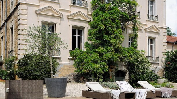 A large, classical building with a swimming pool and lounge chairs in front.