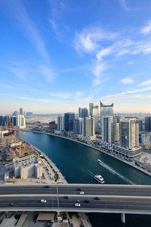 A high-rise building with a river in the foreground and a bridge in the background. - Luxury Studio with Canal View Near Downtown Dubai (Dubai)