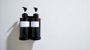 Zwei schwarze Flaschen mit Haar- und Duschgel, jeweils mit Dosierpumpe, Beschriftung und einem Volumen von 200 ml, an einer weißen, gefliesten Wand befestigt.