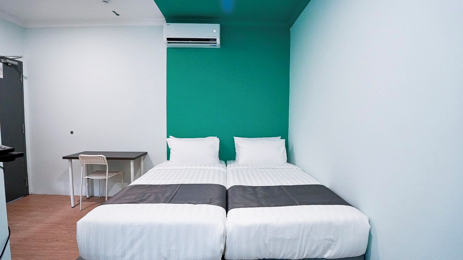 Habitación pequeña con cama individual, escritorio y silla, ropa de cama blanca y una pared de acento color turquesa.