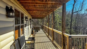 A wooden porch with a bench and a table, overlooking a forested area. - Starry Night - Awesome Views, Hot Tub, Fire Pit! (Sevierville)