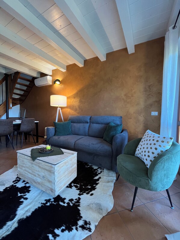 Un salon comprenant un canapé, un fauteuil vert, une table basse, une lampe et un tapis en peau de vache.