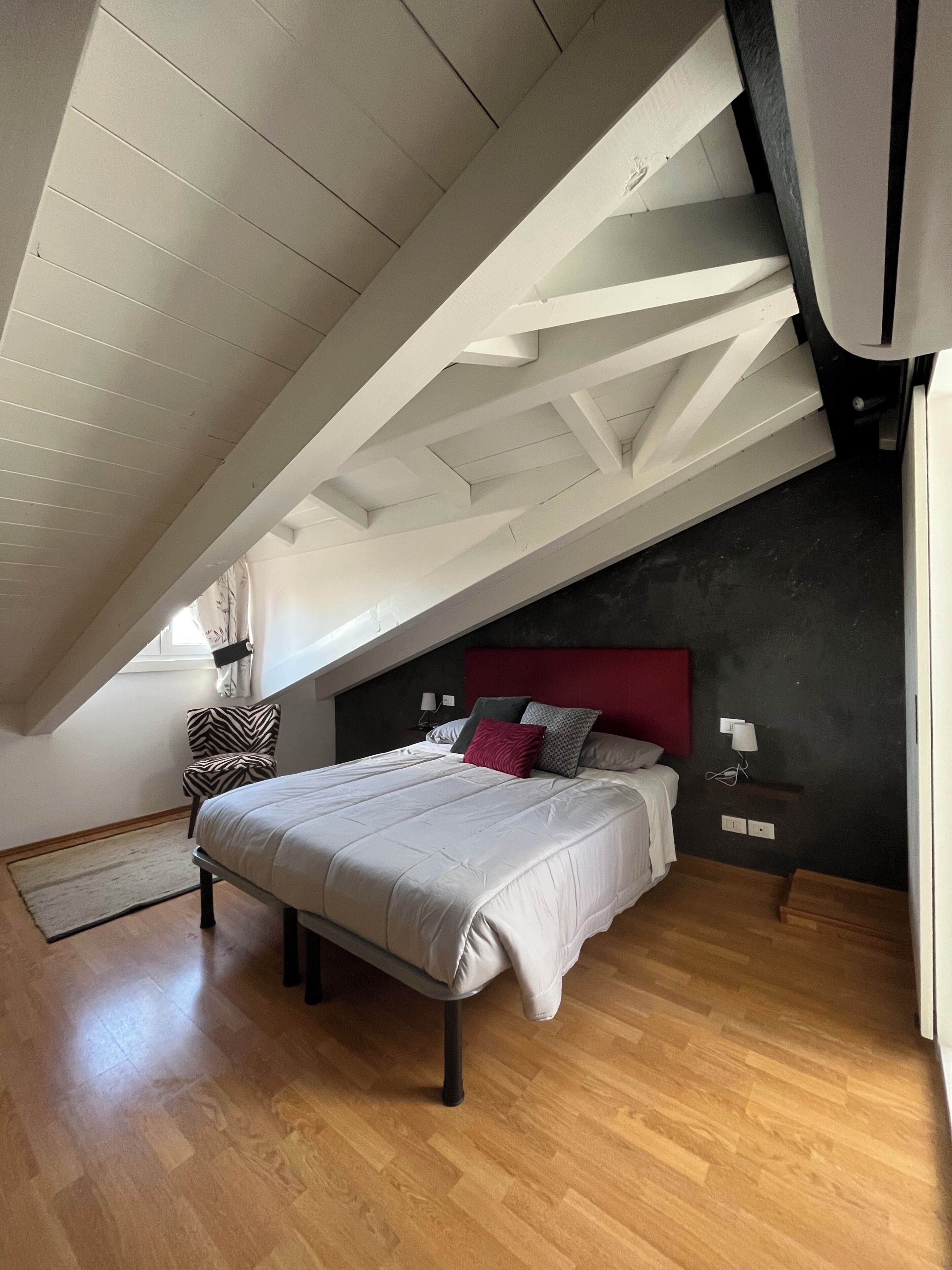 A bedroom with a sloped ceiling, a bed with white bedding, a red headboard, and a wooden floor.