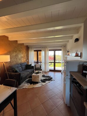 A living room with a sofa, a coffee table, a dining table, and a kitchen area. - SUNSET golf apartment with pool (Castelnuovo del Garda)