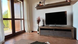Un soggiorno con televisione, mensole in legno, una porta scorrevole in vetro e una candela su un tappeto.