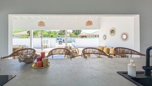 Un vaste espace dédié à la salle à manger, offrant une vue sur un paysage tropical, avec des chaises en osier et un évier de cuisine moderne.