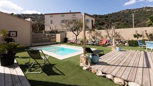 Patio con piscina, césped artificial, terraza de madera y mobiliario exterior.