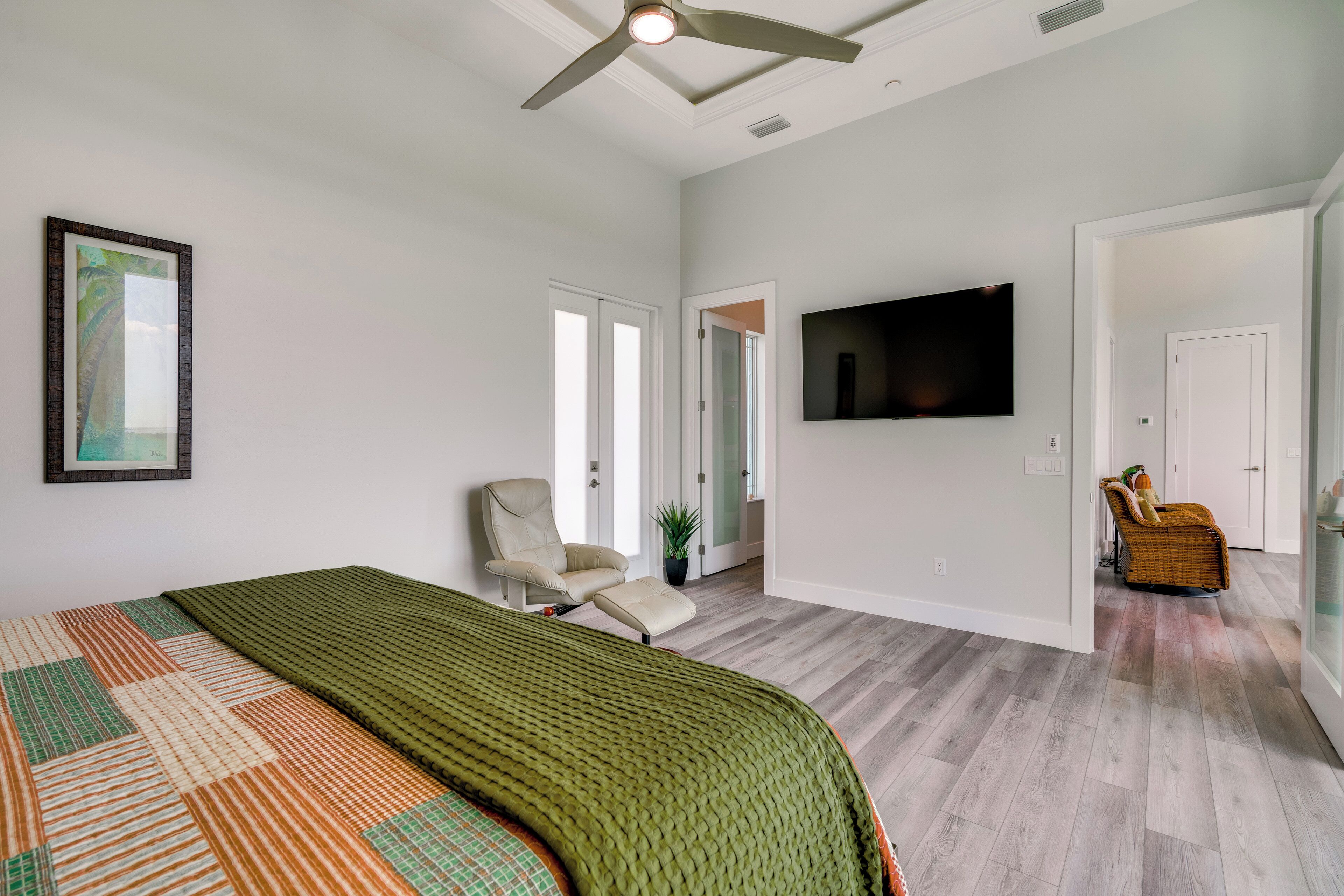 A spacious bedroom with a large bed, a ceiling fan, a flat-screen TV, and a view into the adjacent bathroom.