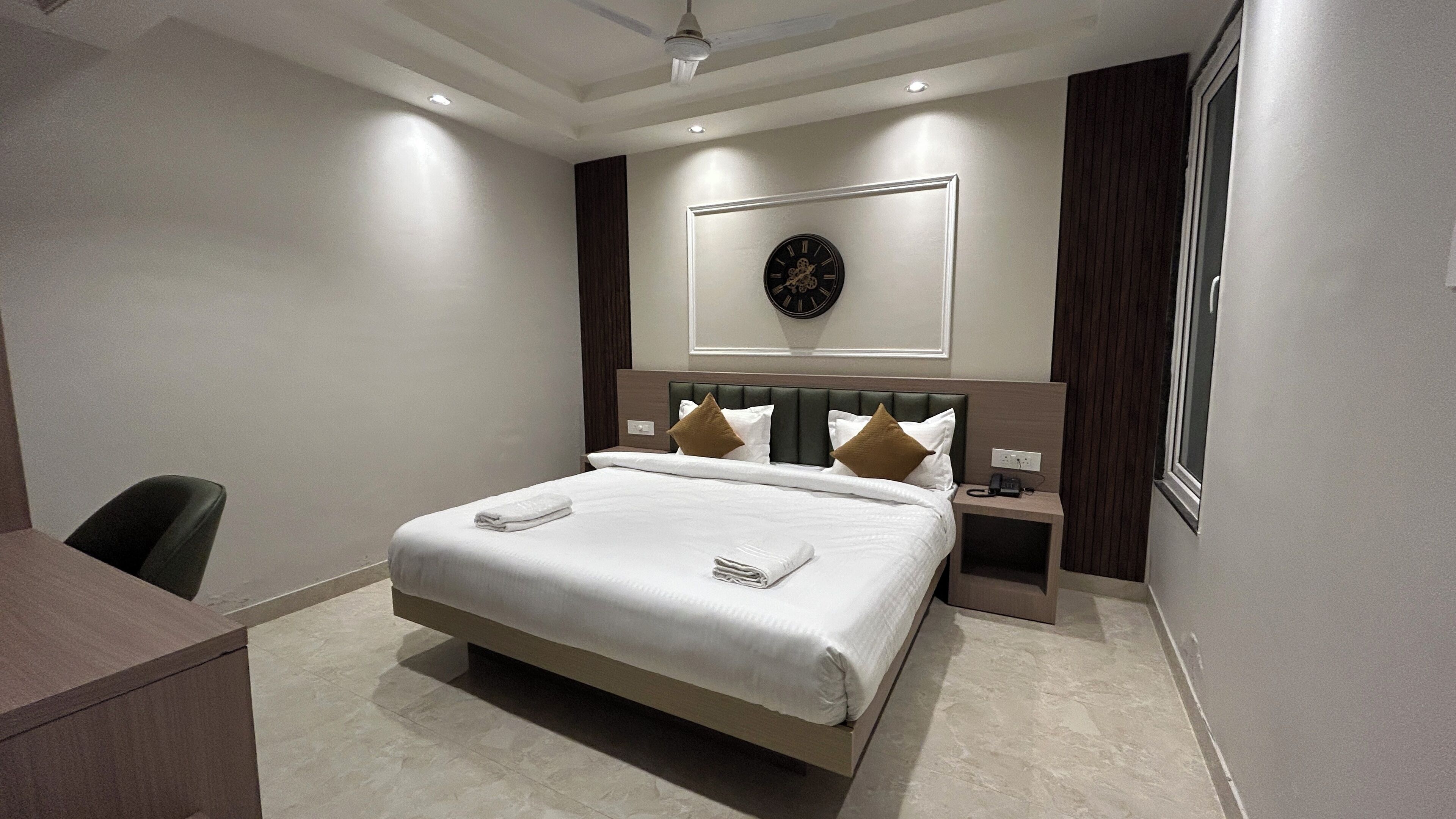 A modern hotel room with a large bed, a desk, and a clock on the wall.