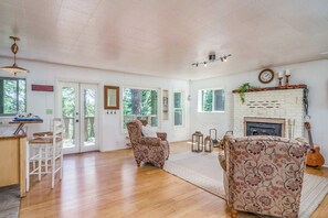 A spacious living room with a fireplace, wooden flooring, and a large window.