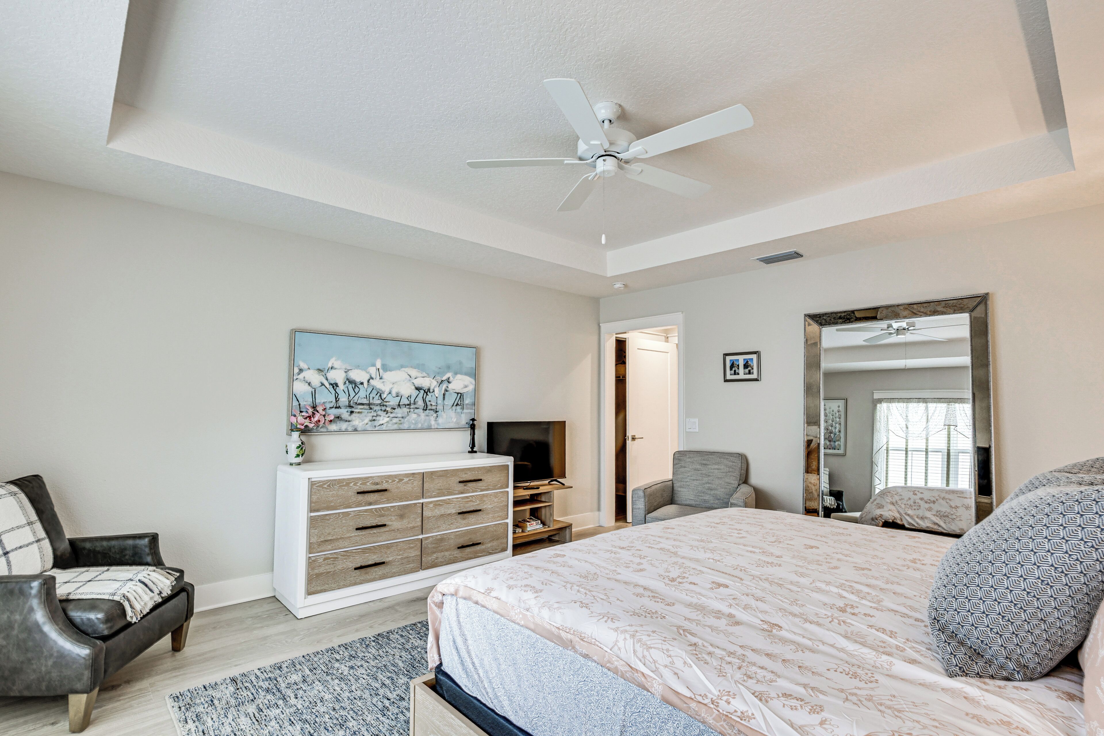 A bedroom with a bed, a dresser, a TV, a chair, and a ceiling fan.