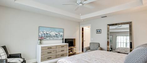 A bedroom with a bed, a dresser, a TV, a chair, and a ceiling fan.