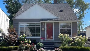 A two-story house with a red front door, large windows, and a small porch area. - Mid-century Family Bungalow: Desirable Birmingham! (Birmingham)