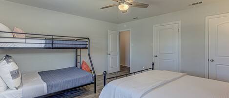 Une chambre avec des lits superposés, un ventilateur de plafond et une porte donnant sur une autre pièce.