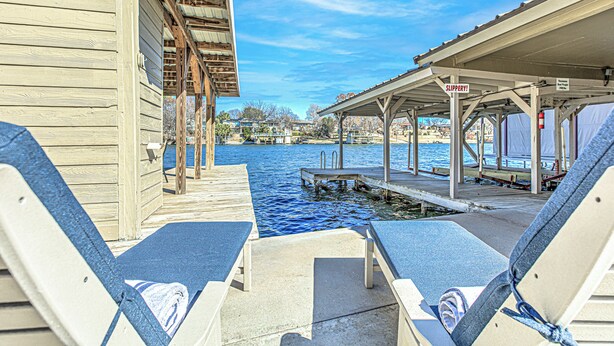 A wooden dock extending into a body of water with lounge chairs and a covered seating area. - Deep Water Dock & Slip: Lake LBJ Getaway (Kingsland)
