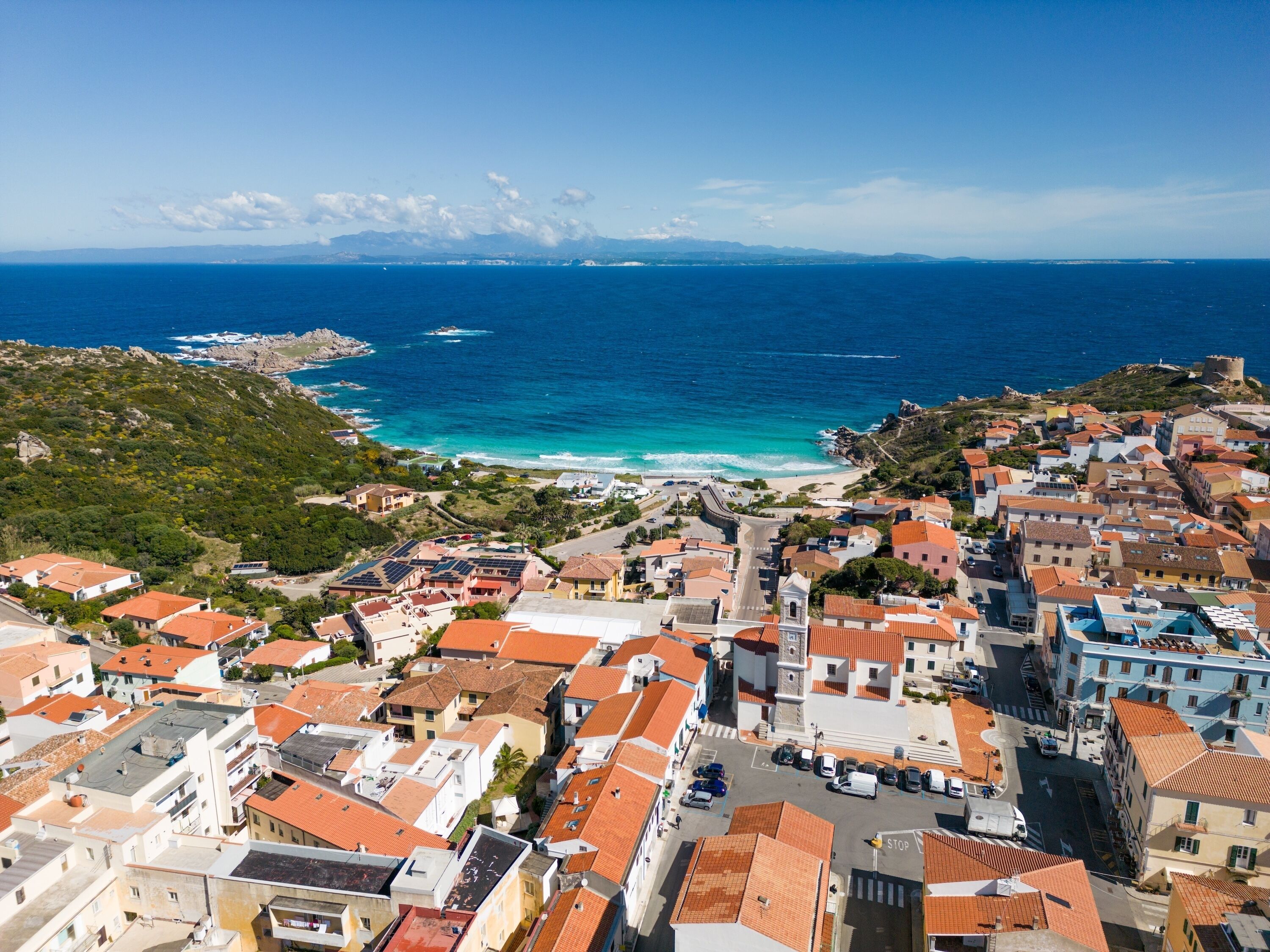 A coastal town with terracotta-roofed buildings, a beach, and a historic fort.