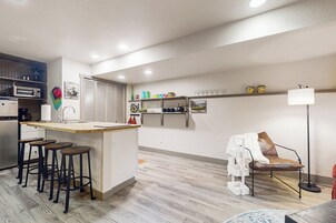 A modern kitchen with a central island, bar stools, a dining area with a chair, and a floor lamp.