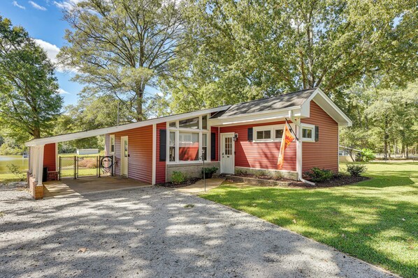 A red single-story house with a covered porch, a small front yard, and a flagpole. - Lakeside Bungalow at Cedar Pines Lake (Lancaster)