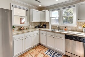 A modern kitchen with white cabinets, a stainless steel refrigerator, a dishwasher, and a window with a view of trees. - Lakeside Bungalow at Cedar Pines Lake (Lancaster)