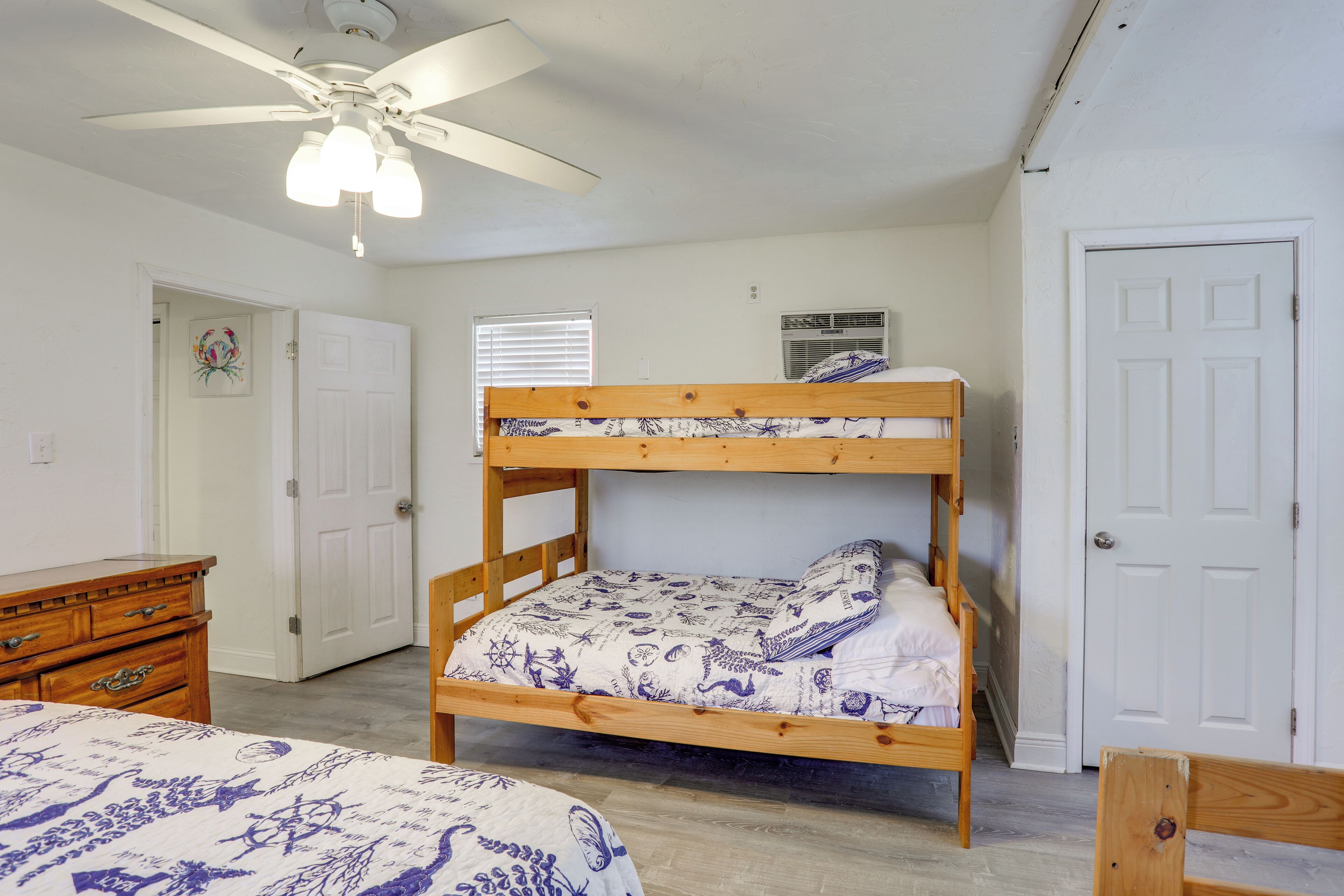 A bunk bed with a patterned bedspread, a wooden dresser, a ceiling fan, and a door.