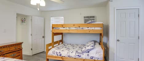 A bunk bed with a patterned bedspread, a wooden dresser, a ceiling fan, and a door.