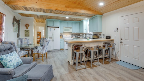 A spacious living area with a grey sofa, a glass coffee table, and a kitchen with light blue cabinets and a wooden ceiling. - 1 Mi to Festivals! Grand Isle Getaway w/ Deck (Grand Isle)