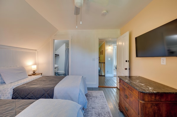 A bedroom with two beds, a dresser, a television, and a bathroom visible through an open door. - Green Mountain Views! Lowell Getaway Near Skiing (Lowell)