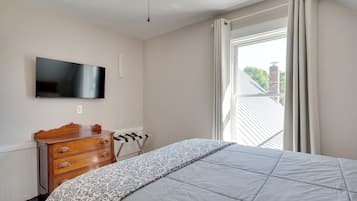 A bedroom with a bed, a wooden dresser, a television mounted on the wall, and a window with curtains.