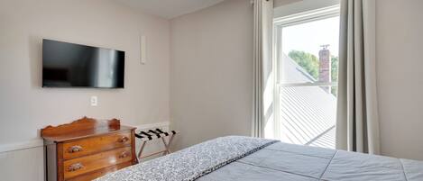 Een slaapkamer met een bed, een houten dressoir, een aan de muur bevestigde televisie en een raam met gordijnen.