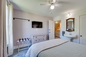 A bedroom with a bed, a television, a ceiling fan, a dresser, and a bathroom with a sink and mirror. - Green Mountain Views! Lowell Getaway Near Skiing (Lowell)