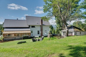 A two-story house with a sloped roof, a front porch with a bench, and a large tree in the yard. - Green Mountain Views! Lowell Getaway Near Skiing (Lowell)