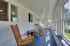A covered porch with white siding, a wooden rocking chair, a small table, and large windows. - Green Mountain Views! Lowell Getaway Near Skiing (Lowell)