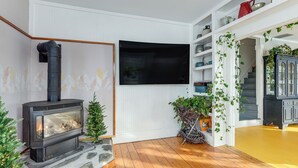 A living room with a fireplace, a TV mounted on the wall, and a staircase leading to another level. - Green Mountain Views! Lowell Getaway Near Skiing (Lowell)