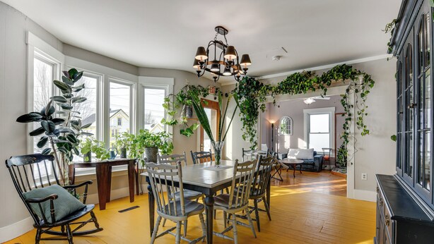 A dining area with a wooden table and chairs, surrounded by large windows and indoor plants. - Green Mountain Views! Lowell Getaway Near Skiing (Lowell)