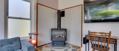Un salon chaleureux avec un poêle à bois, un canapé confortable, un fauteuil en bois et un téléviseur à écran plat fixé au mur.