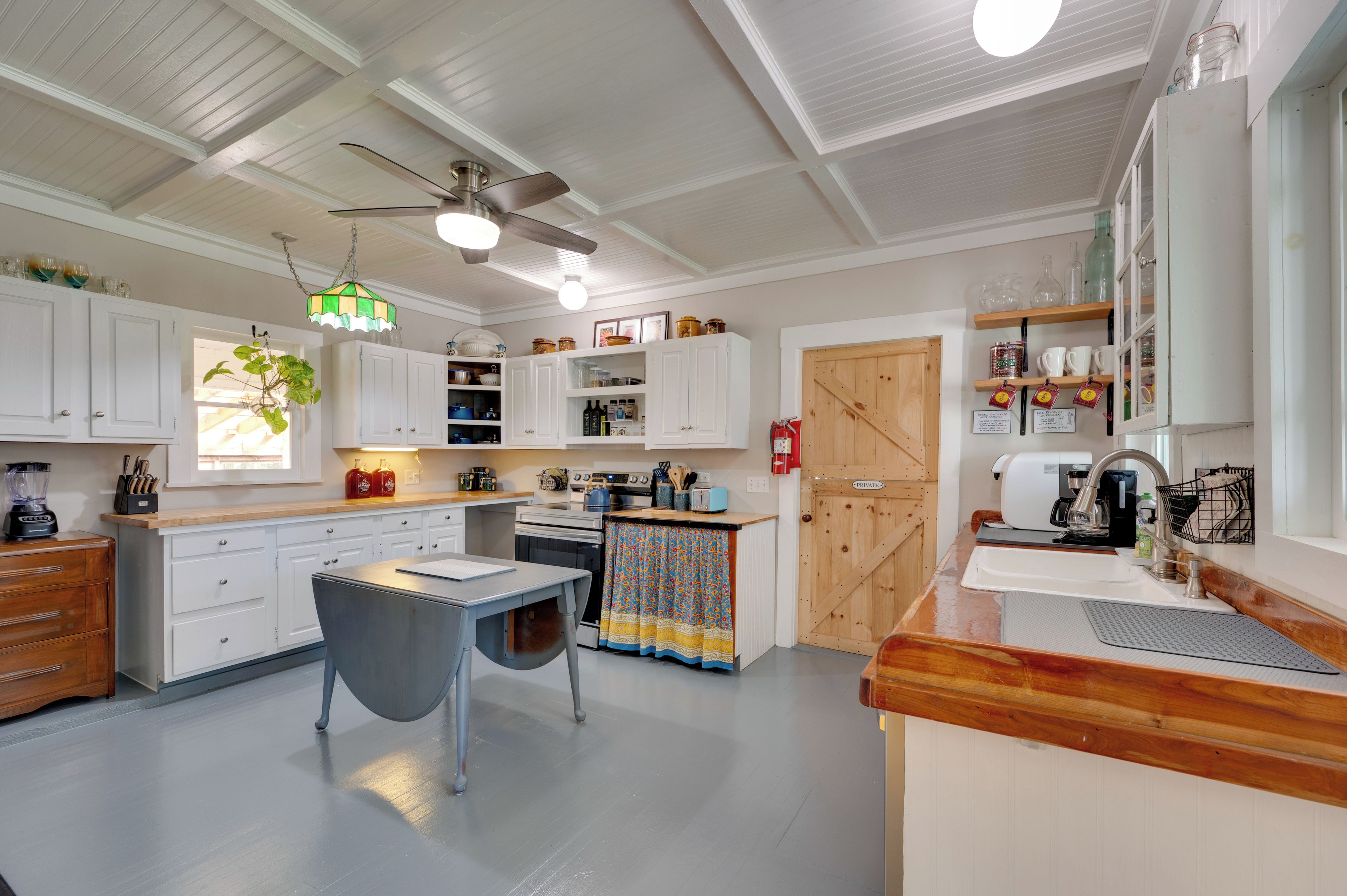 Una cocina con armarios blancos, encimera de madera, una mesa de comedor y un ventilador de techo.