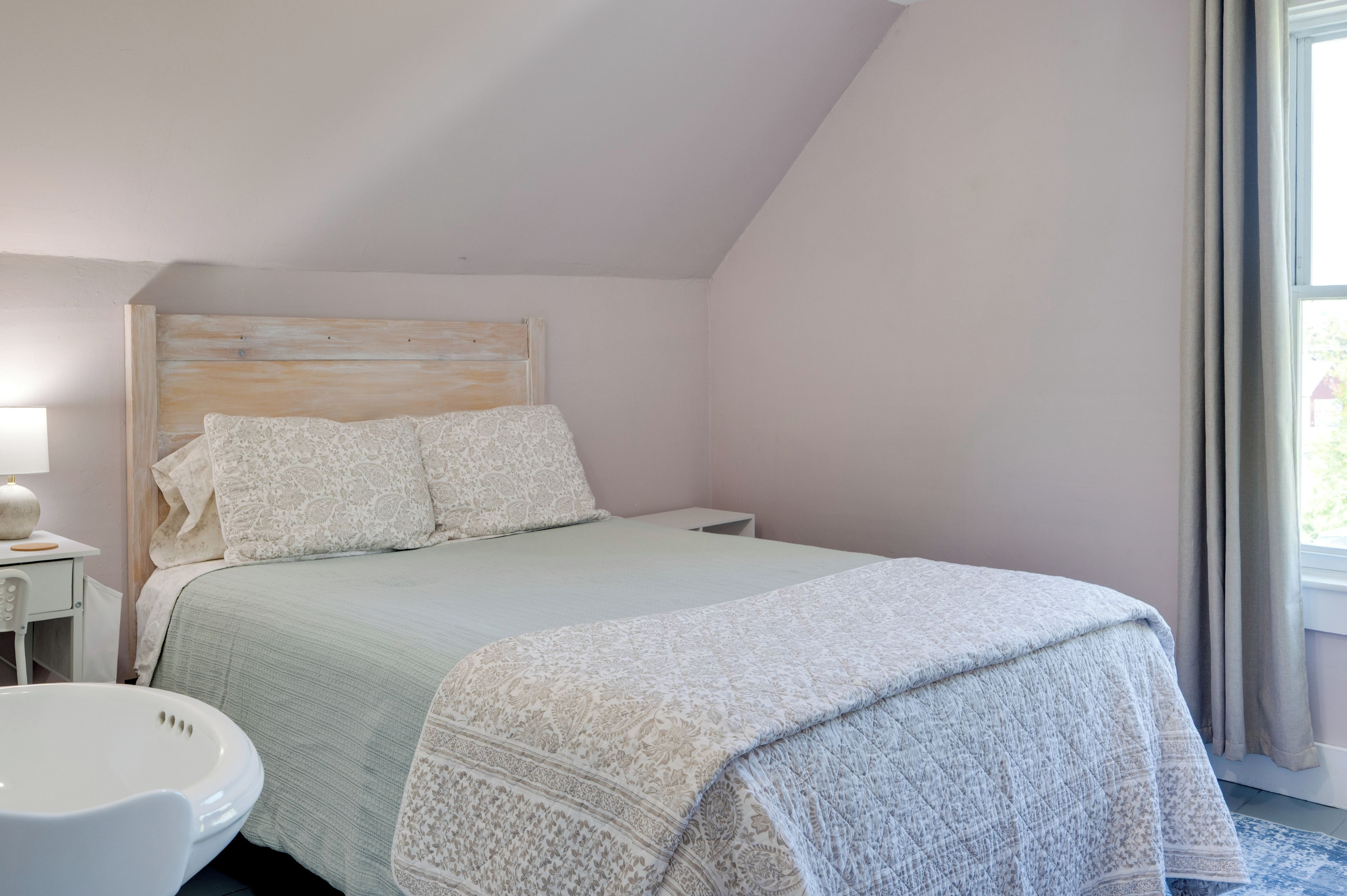 A bedroom with a single bed, a bedside table, a lamp, and a window with curtains.