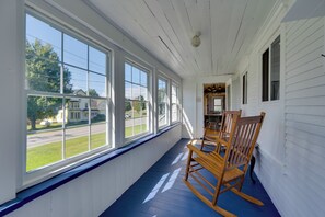 A covered porch with large windows, wooden rocking chairs, and a view of a street and houses. - Green Mountain Views! Lowell Getaway Near Skiing (Lowell)