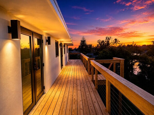 Eine Holzterrasse mit Glastüren, einem Geländer und Blick auf den Sonnenuntergang.
