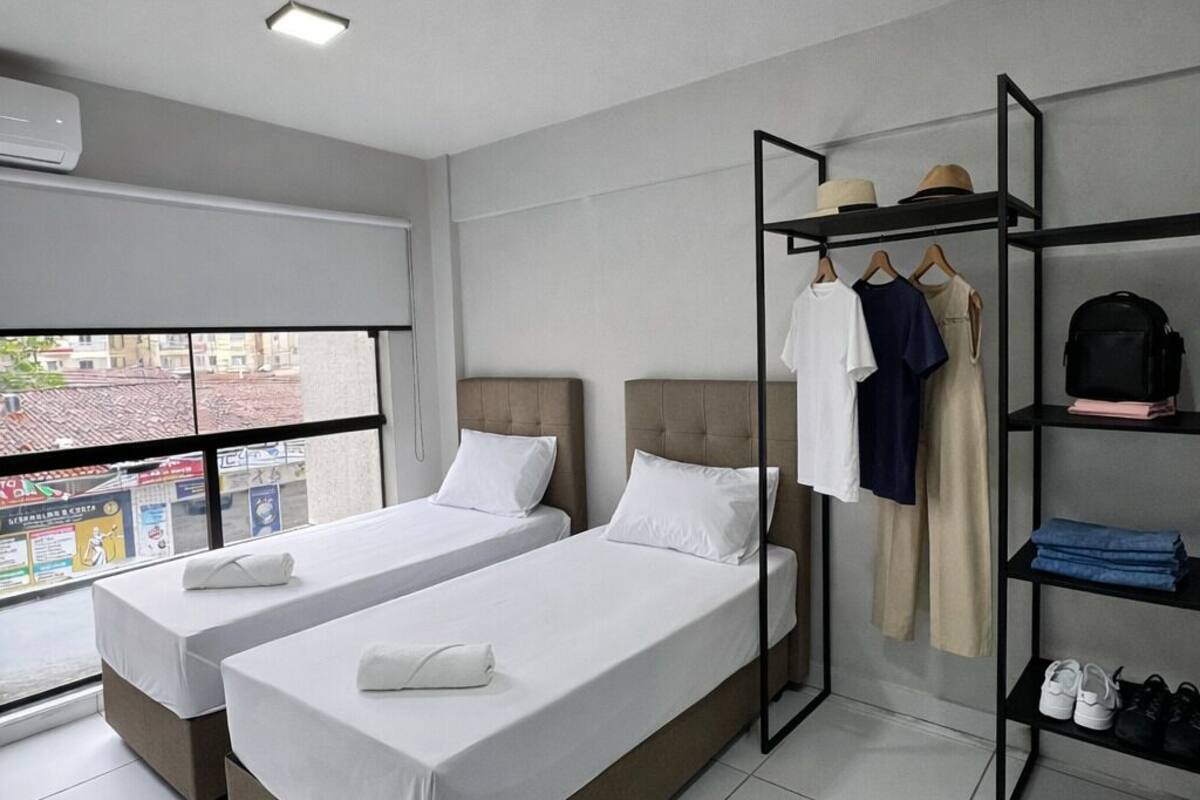 A hotel room with two beds, a wardrobe, a shoe rack, and a window with a city view.