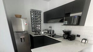A modern kitchen with a stainless steel refrigerator, a microwave, a coffee maker, and a sink. There are two wooden stools and a white speckled countertop. - Villa Continental-Ideal for families-Strategic location in Nicoya Guanacaste (Nicoya)