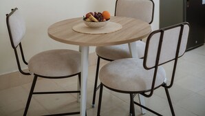 Comedor con una mesa redonda, dos sillas, un cuenco de fruta y adornos tejidos en la pared.