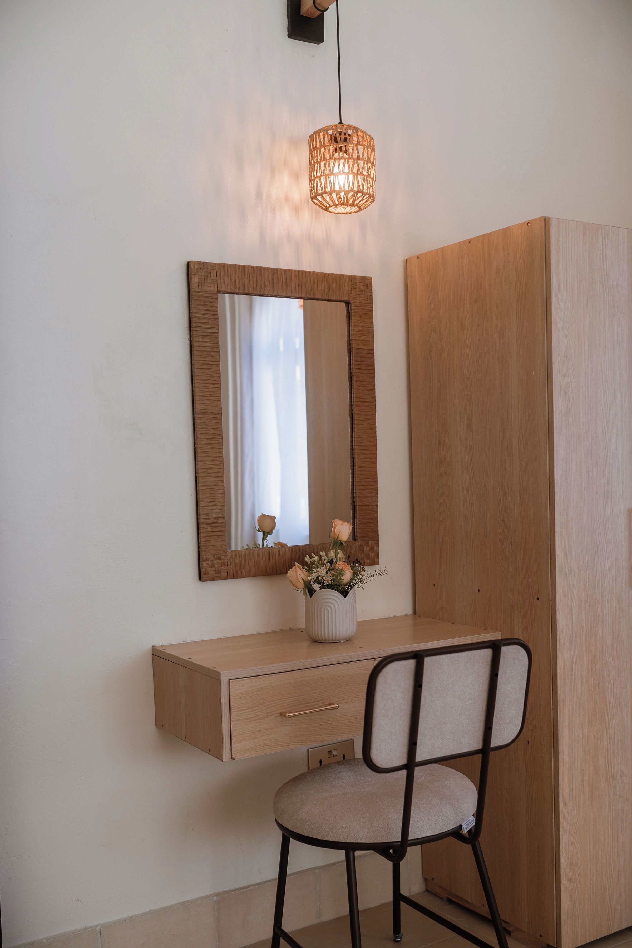 Un tocador de madera con un espejo, un jarrón pequeño con flores y una silla.