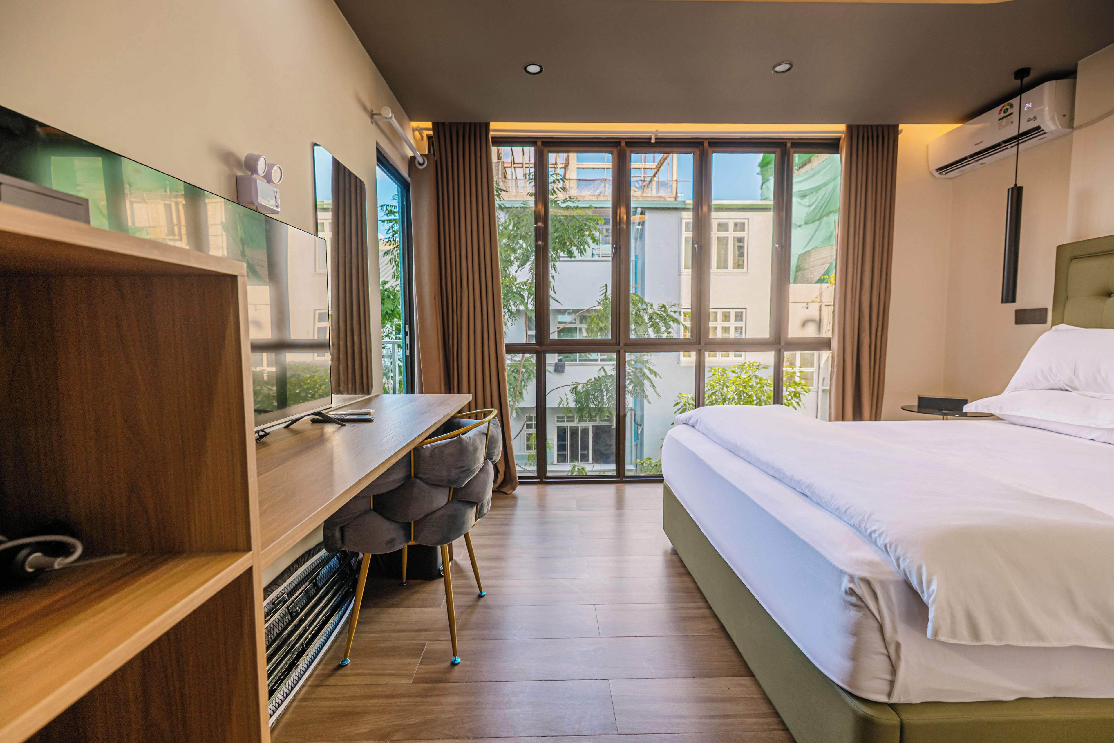 Une chambre d’hôtel moderne dotée d’un grand lit, d’un bureau avec une chaise et offrant une vue sur la ville grâce à de grandes fenêtres.