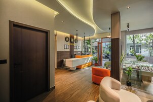 A reception area with a wooden door, a reception desk, a seating area with an orange chair, and a glass display case with plants.