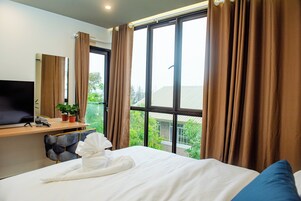 Habitación de hotel con cama, escritorio con ordenador, televisor y ventana con cortinas.