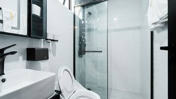 Un baño moderno con cabina de ducha de vidrio, inodoro blanco y lavamanos negro.