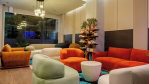 Ein modernes Wohnzimmer mit mehreren Sofas in verschiedenen Farben, einem großen Fenster und einem dekorativen Regal für Pflanzen.