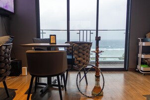 Una habitación con vista al océano, un narguile, una mesa con sillas y un televisor montado en la pared.
